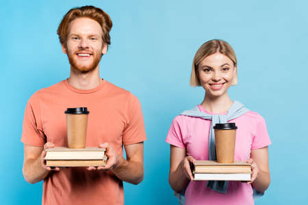 young students holding books and paper cups on blue