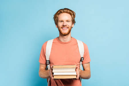 redhead student holding books and looking at camera on blueの写真素材