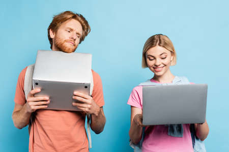 young blonde and redhead students using laptops on blue