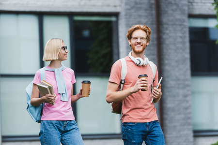young students holding coffee to go, digital tablet and books outsideの写真素材