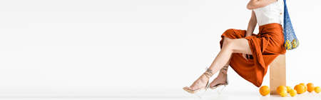 cropped view of elegant woman posing with string bag near scattered citrus fruits on white...