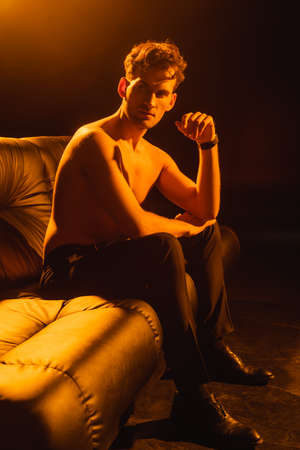 muscular man looking away while sitting on sofa of blackの写真素材