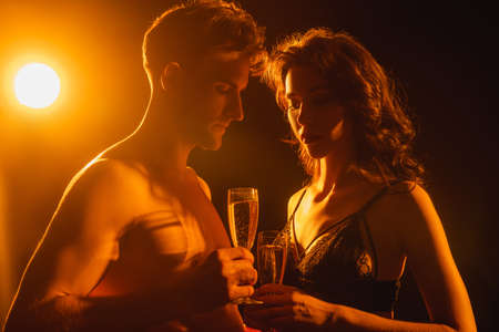 sexy couple holding glasses with champagne on black with back lightの写真素材