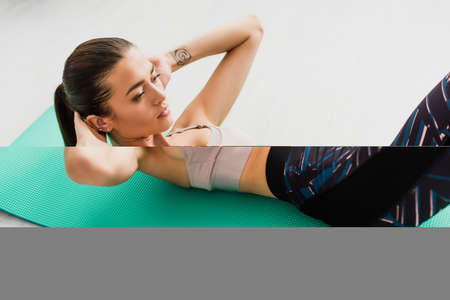 Selective focus of brunette sportswoman doing abs on fitness mat on floorの写真素材