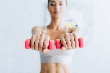 Selective focus of sportswoman training with dumbbells at homeの写真素材