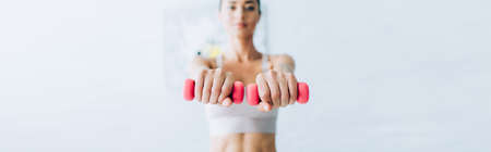 Panoramic crop of sportswoman exercising with pink dumbbells in living roomの写真素材