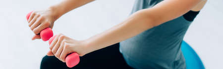 Panoramic shot of pregnant sportswoman exercising with fitness ball and pink dumbbellsの写真素材