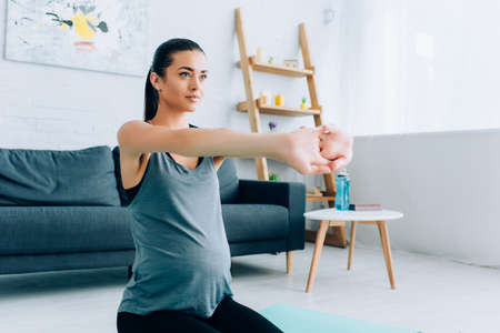 Pregnant woman stretching arms on fitness mat at home