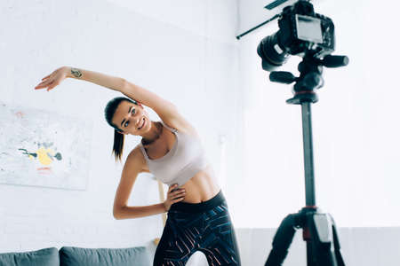 Selective focus of fit sportswoman working out near digital camera at homeの写真素材