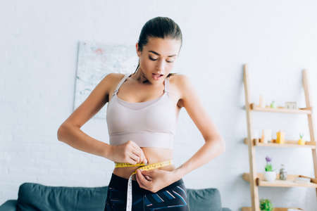 Excited sportswoman measuring waist with tape at homeの写真素材