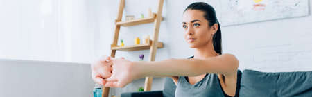 Panoramic shot of brunette sportswoman stretching arms at home