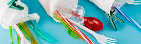 close up view of plastic cups with disposable cutlery on blue background, panoramic shot