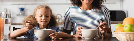 cropped view of african american woman in striped t-shirt having breakfast from bowls, panoramic...