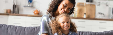 panoramic shot of african american mom with child looking at camera in kitchen