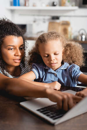 selective focus of african american woman pointing at laptop near concentrated daughter