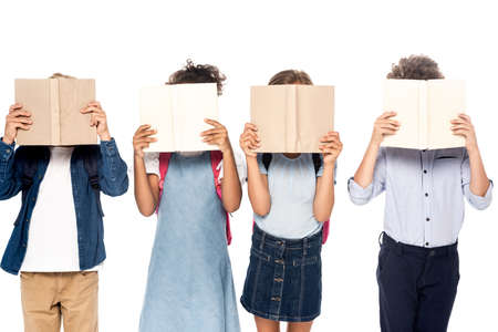 multicultural schoolgirls and schoolboys covering faces with books isolated on white