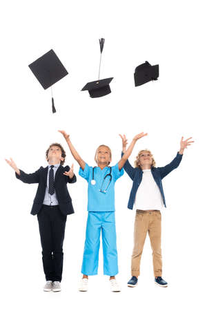 children dressed in costumes of different professions throwing in air black graduation caps isolated on whiteの写真素材