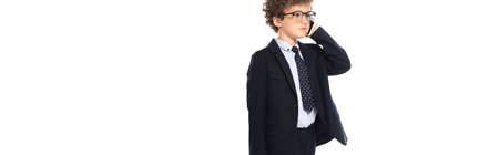 panoramic crop of curly boy in suit and glasses talking on smartphone isolated on whiteの写真素材