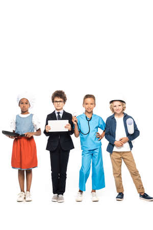 multicultural children in costumes of different professions holding frying pan, blueprint, stethoscope and digital tablet isolated on whiteの写真素材