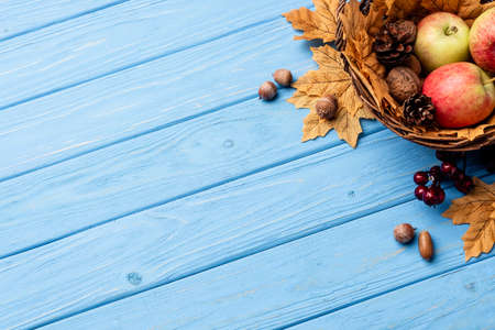 top view of autumnal wicker basket with apples, nuts and cones on blue wooden backgroundの写真素材