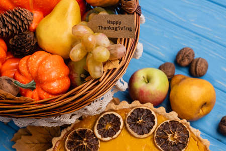 close up view of autumnal harvest in wicker basket with happy thanksgiving card near pumpkin pie on...