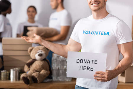 Selective focus of volunteer holding card with donate today lettering and pointing with hand in...