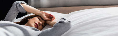 horizontal crop of sad and brunette woman touching face while lying on bedの写真素材