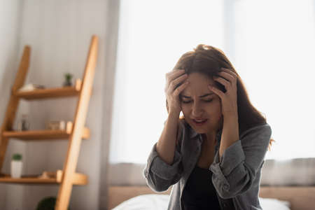 tired woman with closed eyes suffering from pain and touching head at homeの写真素材
