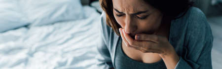 panoramic crop of woman covering mouth while having nausea at homeの写真素材