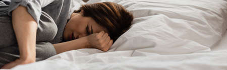 panoramic concept of brunette woman suffering from pain and touching head while lying on bed