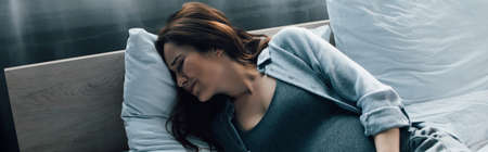 panoramic shot of pregnant woman suffering from pain on bedの写真素材