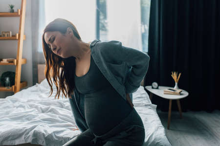pregnant woman having back pain in bedroomの写真素材