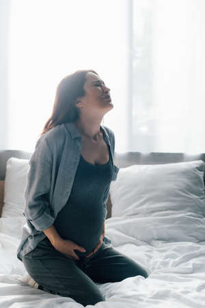 pregnant woman suffering from pain while sitting on bed