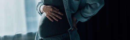 panoramic concept of pregnant woman suffering from pain while touching belly at home