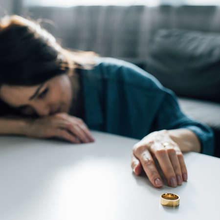 selective focus of sad woman reaching golden ring on coffee table, divorce conceptの写真素材
