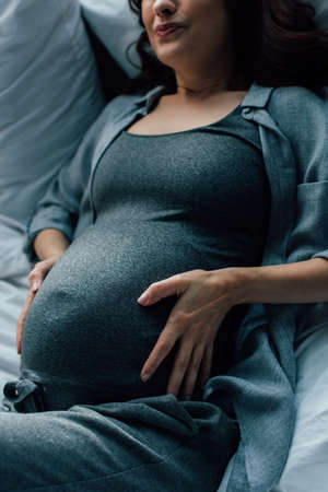 cropped view of pregnant woman suffering from pain on bedの写真素材
