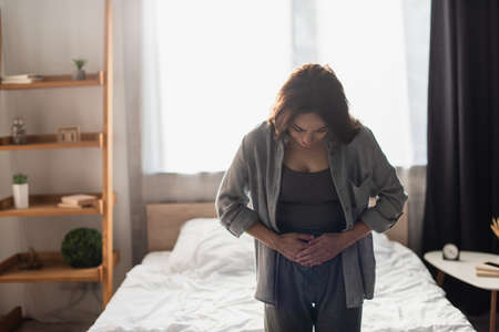 woman suffering from stomach ache in modern bedroomの写真素材