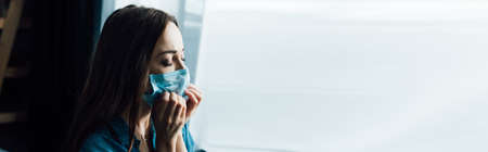 panoramic shot of brunette woman touching medical mask at homeの写真素材