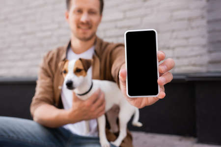 Selective focus of man showing smartphone with blank screen and embracing jack russell terrier on...