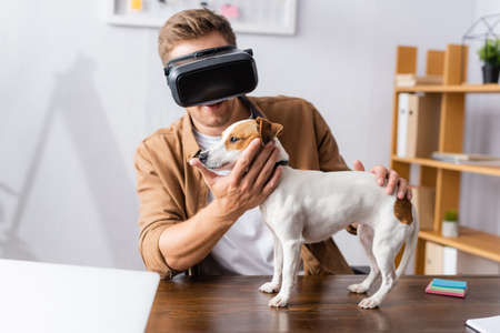 young businessman in vr headset touching jack russell terrier dog standing on office deskの写真素材