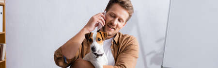 horizontal concept of businessman talking on mobile phone and holding jack russell terrier dog