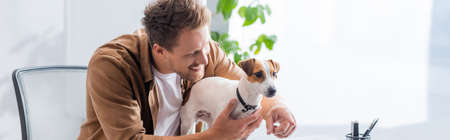 panoramic shot of young businessman pointing with finger near jack russell terrier dog in officeの写真素材