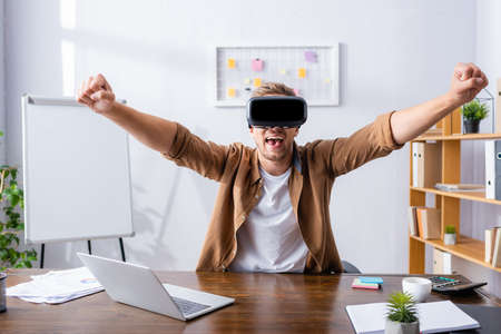 excited businessman in vr headset showing winner gesture at workplace