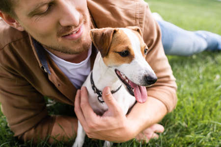 partial view of young man cuddling jack russell terrier dog while relaxing on green grassの写真素材