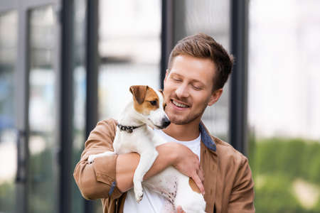 young man holding white jack russell terrier dog with brown sports on headの写真素材