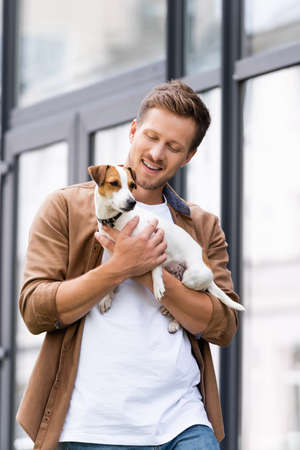 man in casual clothes holding white jack russell terrier dog with brown spots on headの写真素材