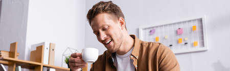 Panoramic crop of young businessman holding cup of coffee in officeの写真素材