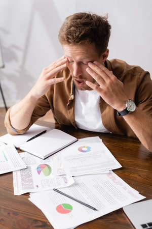 Selective focus of tired businessman looking at documents near laptop on tableの写真素材
