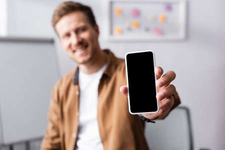 Selective focus of businessman showing smartphone with blank screen in office