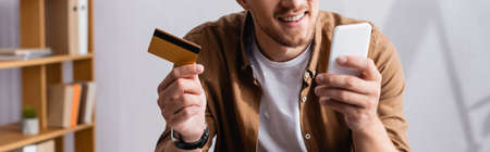 Panoramic shot of businessman using smartphone and credit card in office